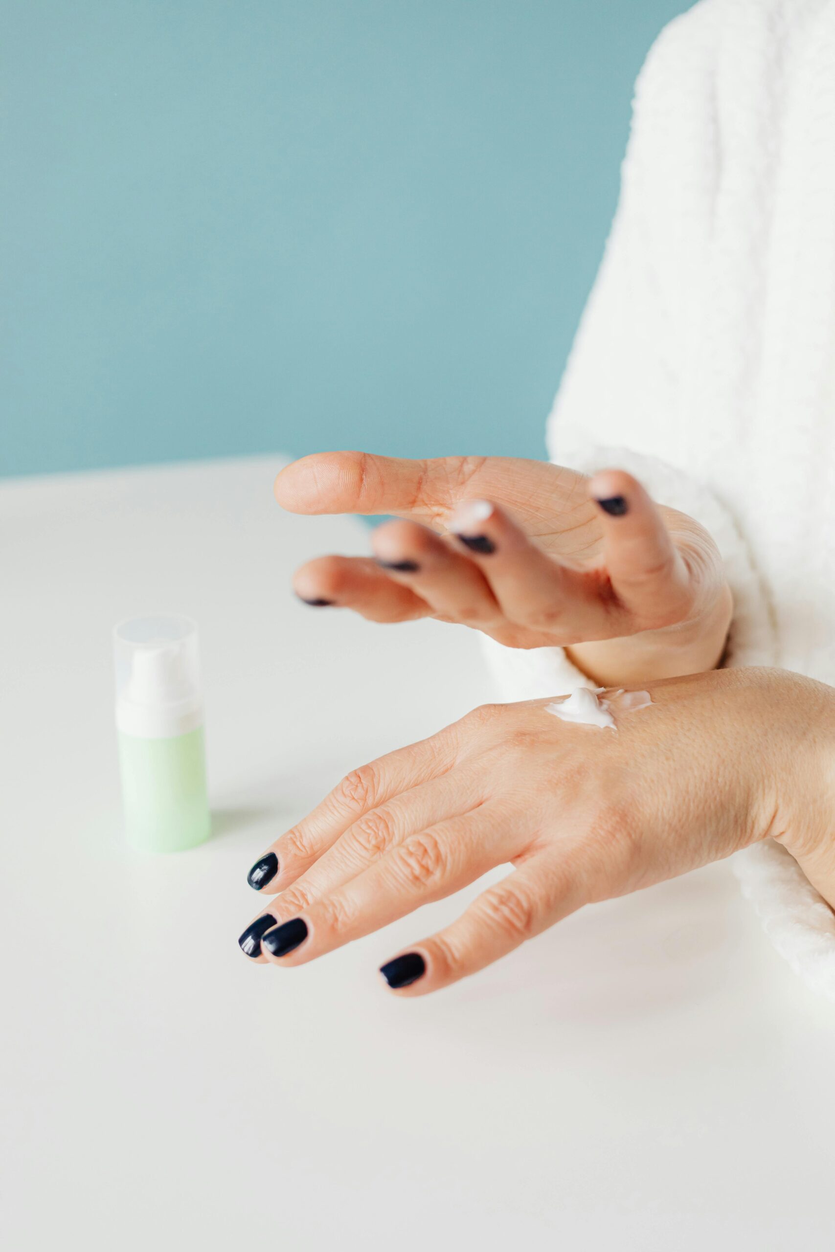 Close-up of hands with painted nails applying hand cream in a well-lit setting.